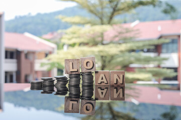 Stacked coins and the word LOAN on the glass table. Trees, and housing development in the background. 