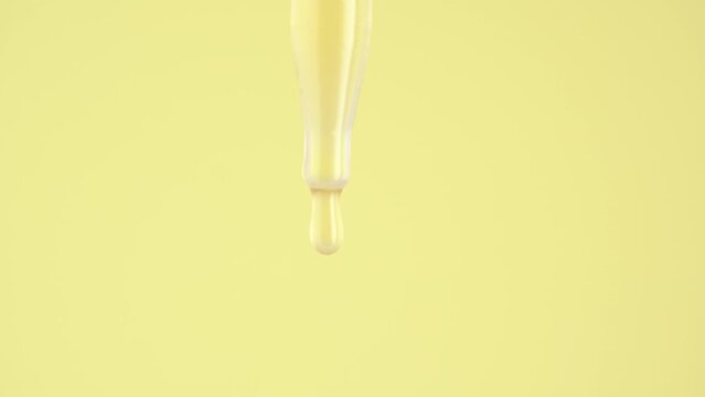 Close-up glass dropper with cosmetic serum on a yellow background. Essential oil, body serum, drops drip. Drops of serum or essential oil fall from a glass pipette.
