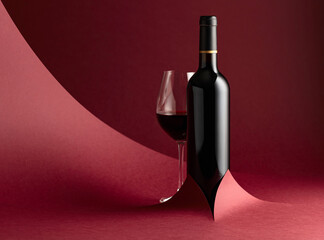 Bottle and glass of red wine on a red background. - 778049239