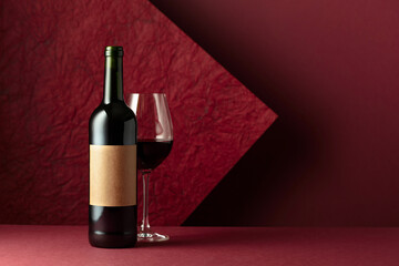 Bottle and glass of red wine on a red background.