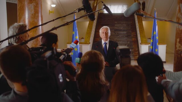 Senior EU representative answers press questions and gives interview for TV breaking news in parliament hall. Serious political speech during press conference. Campaign speech. Political discourse.