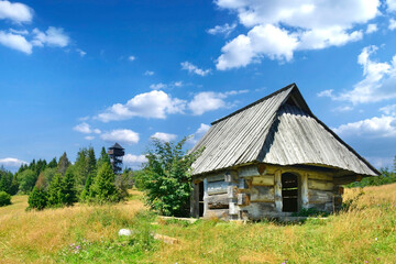 Fototapeta na wymiar Old wooden shepherd's hut and lookout wooden tower on Magurki peak in Gorce mountains, Poland. Summer sunny day in mountains.