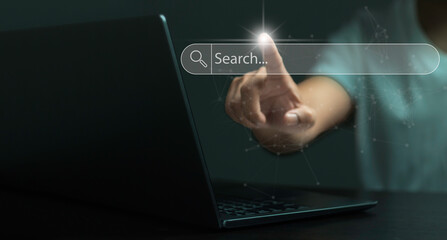 A person is pointing at a laptop screen with a search bar