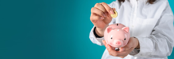 A woman puts a penny in a piggy bank, studio background