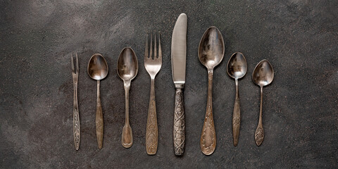 Old vintage cutlery in a row on a dark grunge background. Top view, flat lay. Banner