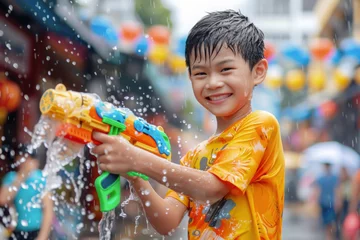 Foto op Plexiglas Happy traveler asian boy wearing summer shirt holding colorful squirt water gun over blur city, Water festival holiday concept © grapestock