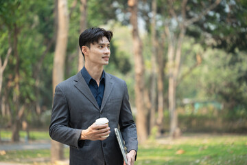 Handsome businessman with takeaway coffee standing in the urban park