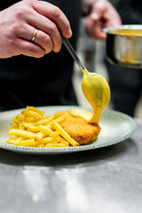A skilled chef meticulously adds sauce to a dish of schnitzel and fries, showcasing culinary artistry.