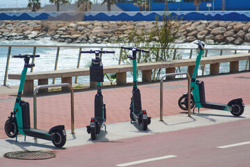 Electric scooters parked along the railing of a boardwalk, with the ocean and rocks in the...