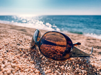 Summer vacation concept, sunglasses on sea sand, seashore, seaside, ocean beach. Mediterranean sea. Beautiful sea side, summer beach in sunrise lights, waves. Beach, coast line, Nature