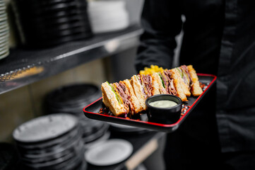 A server presents a delicious sandwich, cut and arranged on a red plate with sauce, showcasing the art of culinary presentation.