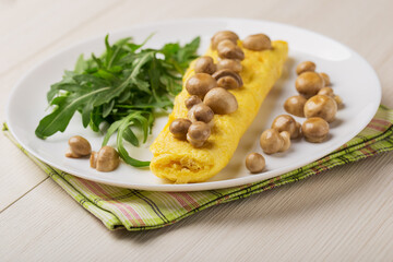 Close up French three eggs omelette with mushrooms, arugula for a breakfast on a white plate on wooden background. Low carb diet.
