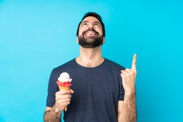 Young man with a cornet ice cream over isolated blue background pointing up and surprised - obrazy, fototapety, plakaty