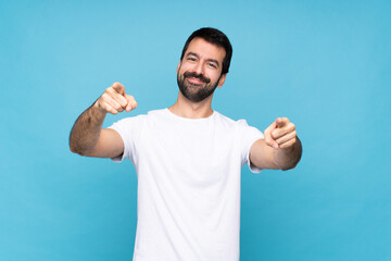 Young man with beard  over isolated blue background points finger at you while smiling