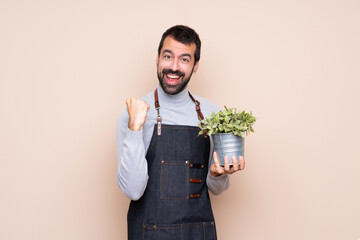 Man holding a plant over isolated background celebrating a victory in winner position