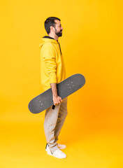 Full-length shot of man over isolated yellow background with a skate
