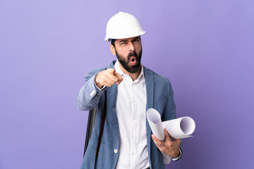 Young architect man with helmet and holding blueprints over isolated purple background frustrated and pointing to the front - 778099271