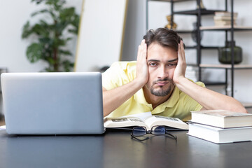 Tired and bored student sitting at the desk while preparing for exams at university	