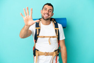 Young mountaineer caucasian man with a big backpack isolated on blue background counting five with...