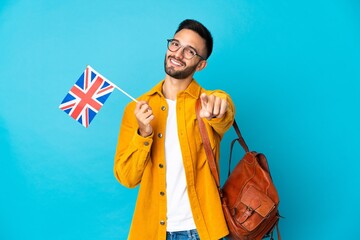 Young caucasian man holding an United Kingdom flag isolated on yellow background pointing front...