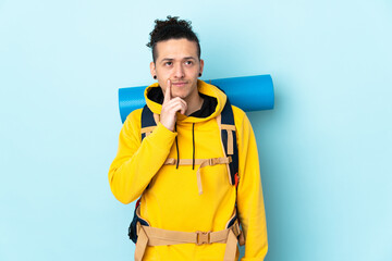 Young mountaineer man with a big backpack over isolated blue background thinking an idea