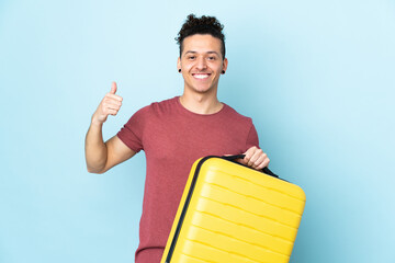 Caucasian man over isolated blue background in vacation with travel suitcase and with thumb up