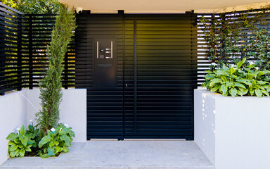 A modern design house entrance with a black painted iron door between white walls at upscale suburbs of Athens. Travel in Greece. - 778115413