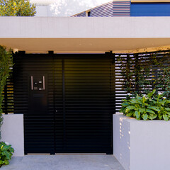A modern design house entrance with a black painted iron door between white walls at upscale suburbs of Athens. Travel in Greece. - 778115495