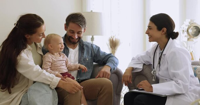 Loving parents and their baby visited paediatrician, sit o sofa lead talk, telling about health complaints to friendly female pediatrist during home-call. Professional medical services, regular check