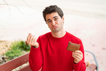 Young handsome man holding a wallet and with sad expression