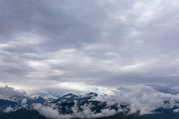 Real mountain landscape. Low clouds over mountains with snowy peaks. Twilight. High point of view