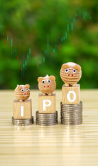 Rows of money coins stacks with IPO word and piggy bank on wooden cube and candlestick charts background for Initial Public Offering, Increased investment concept, economic concept.Vertical.