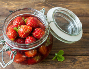 Homemade dessert of canned strawberries in a glass jar on a wooden table. Bursting with strawberry goodness.