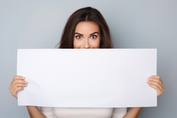 Smiling woman holding a large poster obscuring her face. Blank background.