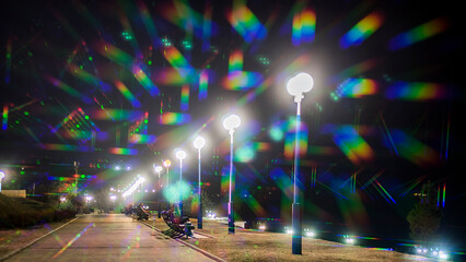 Lots of rainbow colored glare from lanterns on the night sea promenade in summer	
