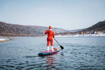 A woman stands on a SUP board and paddles, a man in a red protective suit floats on a board with a...