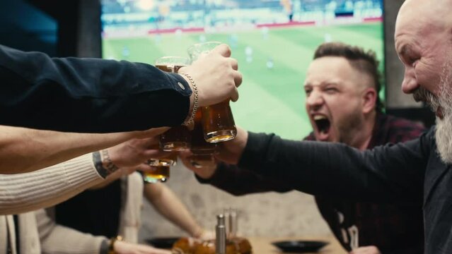 Male friends are watching a football match live, drinking beer and discussing the game, in a bar or sports pub. A group of mature sports fans cheer for their favorite football team.