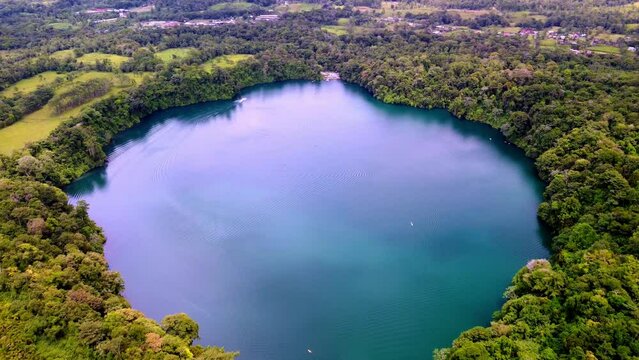 Drone flying above Rio Cuarto Lake surrounded by lush greenery on a sunny day in Costa Rica