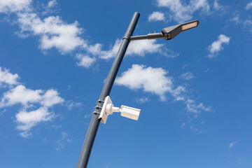 Modern street lamp with surveillance camera in park against the background of a dramatic sky. A...