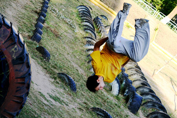A guy does an acrobatic stunt at the stadium with a car tire on the grass and ground against the...
