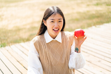 Young Chinese woman with an apple at outdoors with surprise and shocked facial expression