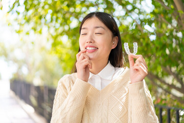 Young Chinese woman at outdoors holding invisible braces with happy expression