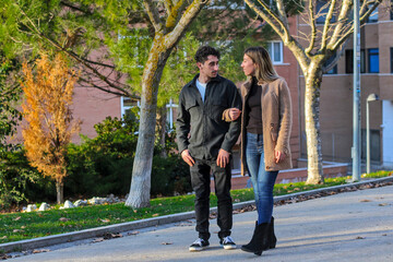 Young white couple walking on the sidewalk, looking at each other and arm in arm