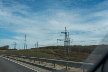 A road with a power line running along it. The sky is blue and there are some clouds