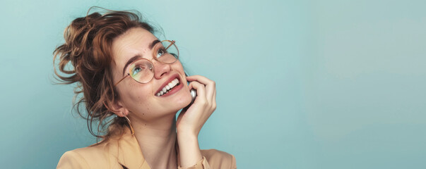 Happy young woman with glasses looking upwards dreamy expression against blue background. Casual fashion, joy and optimism captured in natural light