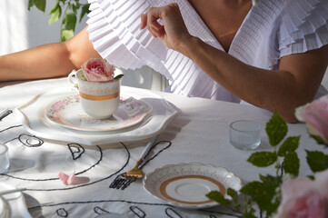 A woman, a girl in a white dress sits at a table and holds a cup of tea or coffee in her hands....