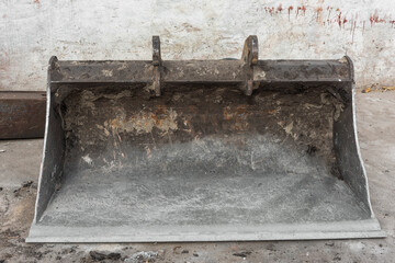 rusty steel shovel bucket of a demolition machine lies on a concrete floor