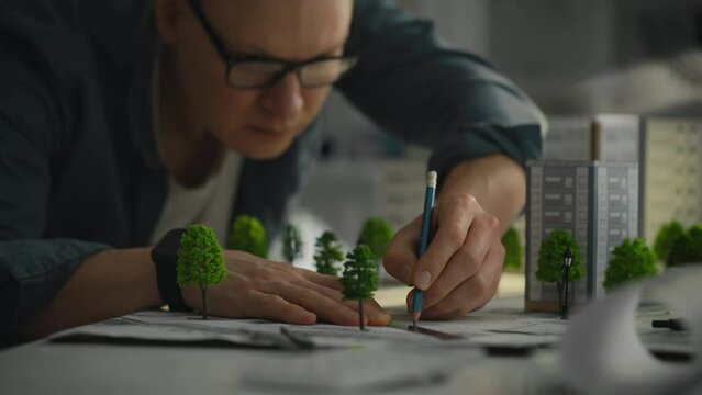 Dressed in a stylish shirt, a blueprint designer in an industrial laboratory carefully uses a pencil to create a design for a green residential area, showing his creativity and professionalism
