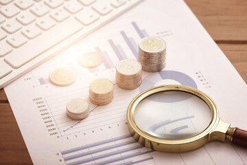 Coins, magnifying glasses, and computer keyboards placed on financial data reports