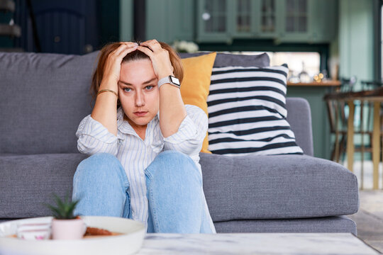 Depressed young woman sitting on living room floor at home